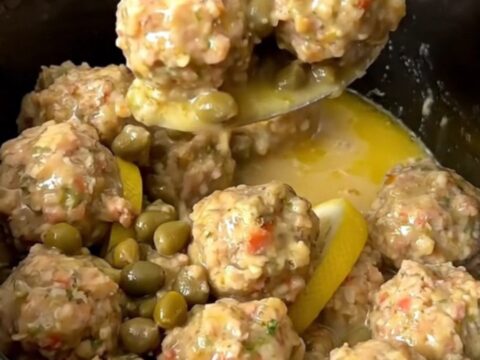 A close-up of tender chicken meatballs in a glossy lemon and caper butter sauce in a slow cooker.