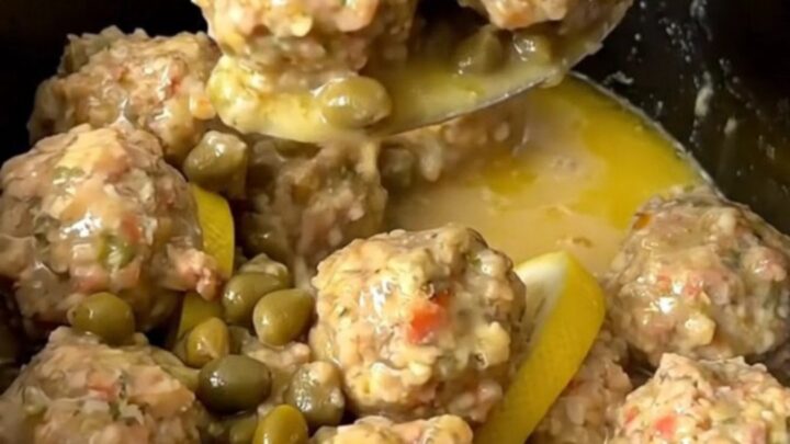 A close-up of tender chicken meatballs in a glossy lemon and caper butter sauce in a slow cooker.