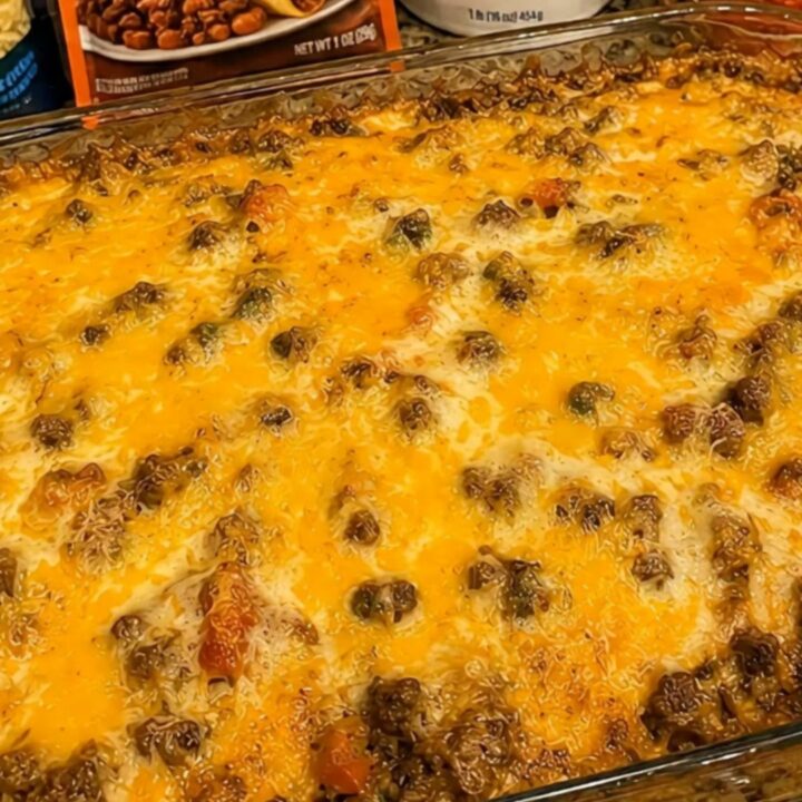 A clear glass baking dish filled with a golden-brown, cheesy loaded taco casserole with visible steam rising.