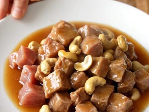 A white slow cooker insert filled with cubes of tender pork loin and whole roasted cashews in a glossy honey soy sauce.