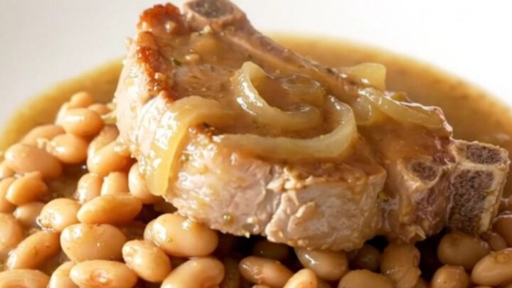 A close-up view of bone-in pork chops and butter beans served on a white plate with a thick onion sauce.
