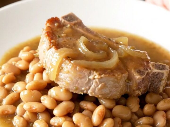 A close-up view of bone-in pork chops and butter beans served on a white plate with a thick onion sauce.