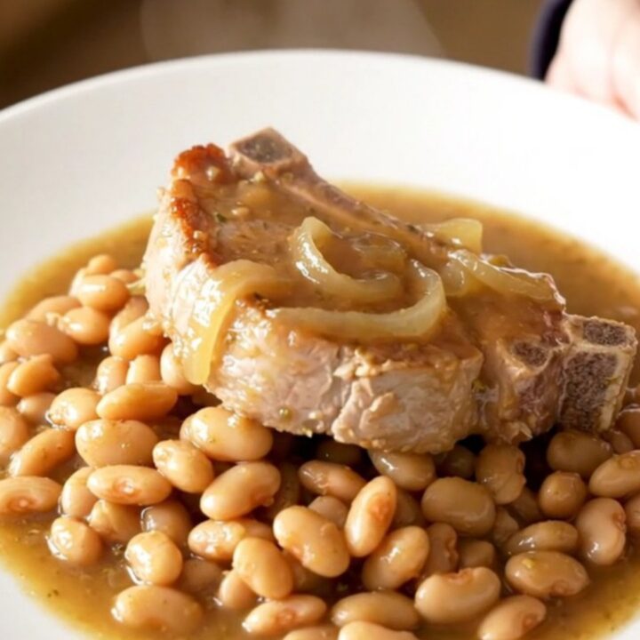 A close-up view of bone-in pork chops and butter beans served on a white plate with a thick onion sauce.