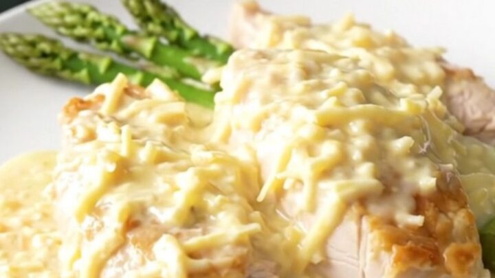 A top-down view of creamy Swiss chicken breasts topped with fresh asparagus in a slow cooker.