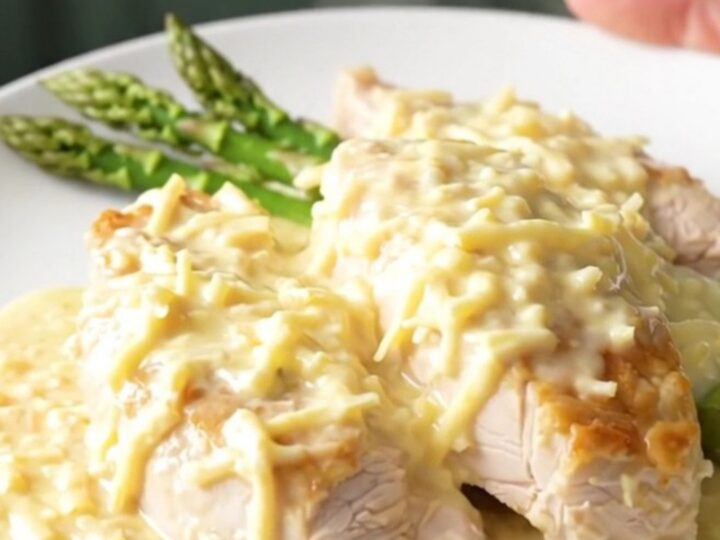 A top-down view of creamy Swiss chicken breasts topped with fresh asparagus in a slow cooker.