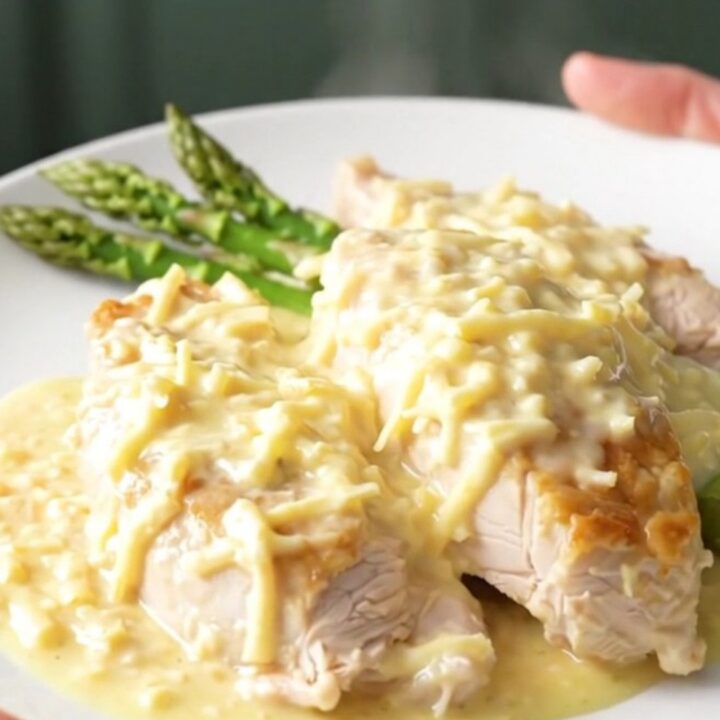 A top-down view of creamy Swiss chicken breasts topped with fresh asparagus in a slow cooker.