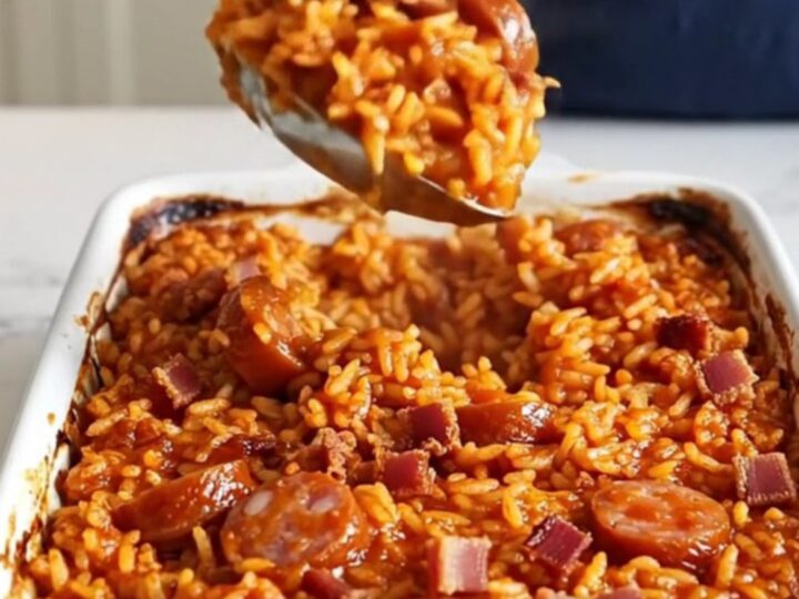 A large white ceramic baking dish filled with Savannah red rice, smoked sausage, and crumbled bacon.
