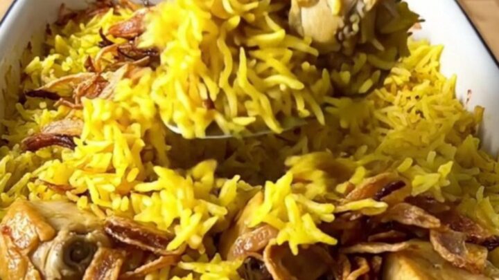 A large rectangular baker filled with golden yellow basmati rice and tender chicken pieces topped with crispy onions.