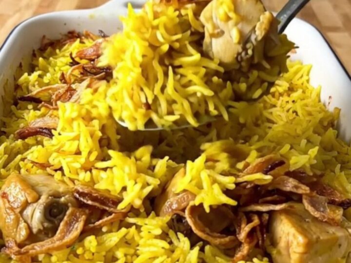 A large rectangular baker filled with golden yellow basmati rice and tender chicken pieces topped with crispy onions.
