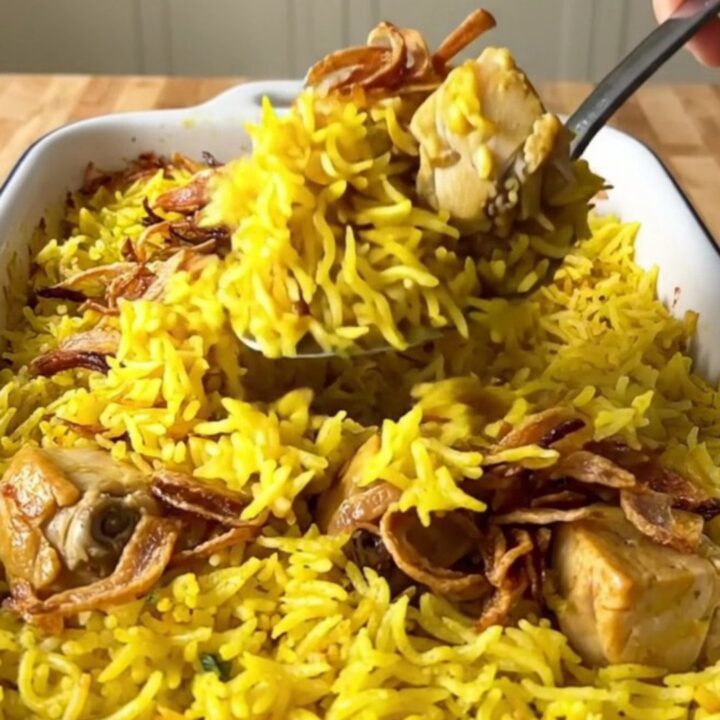 A large rectangular baker filled with golden yellow basmati rice and tender chicken pieces topped with crispy onions.