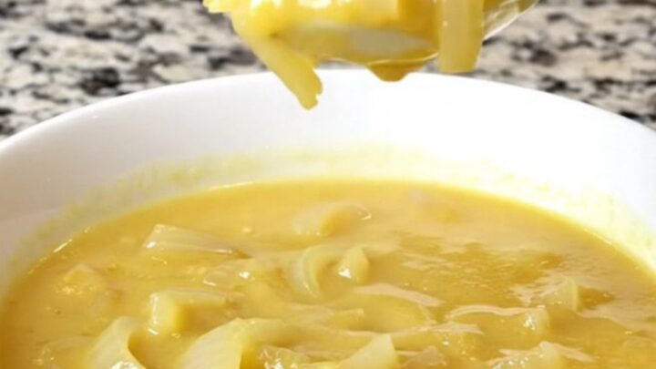 A bowl of creamy cheddar onion soup in a white bowl with soft steam rising.