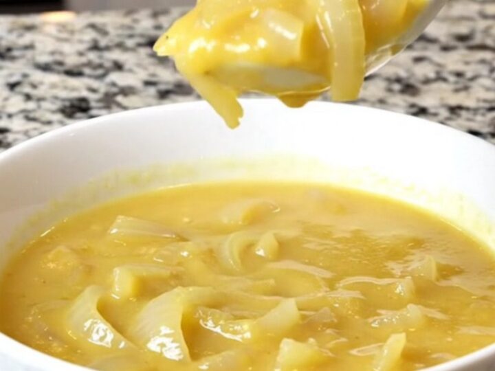 A bowl of creamy cheddar onion soup in a white bowl with soft steam rising.
