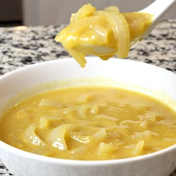 A bowl of creamy cheddar onion soup in a white bowl with soft steam rising.