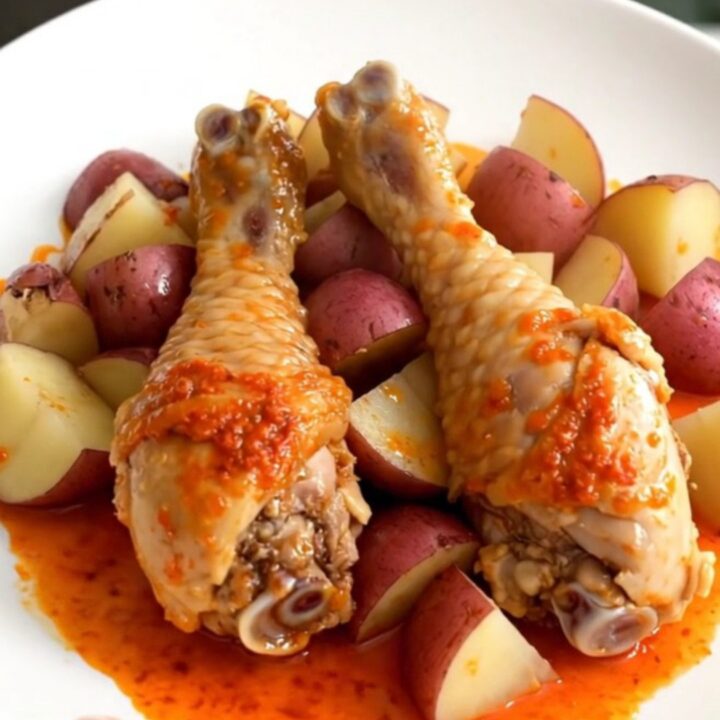 A close-up of tender, skinless chicken drumsticks and quartered red potatoes in a dark slow cooker