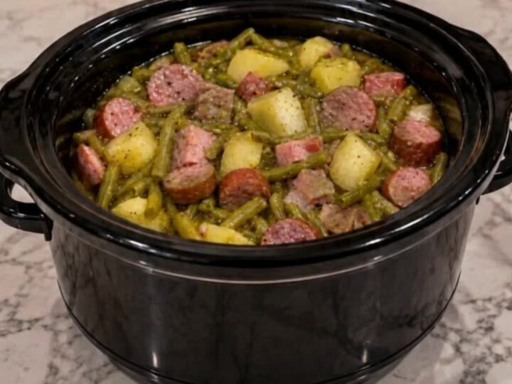 A steaming bowl filled with sliced smoked sausage, tender baby potatoes, and vibrant green beans in a savory broth.