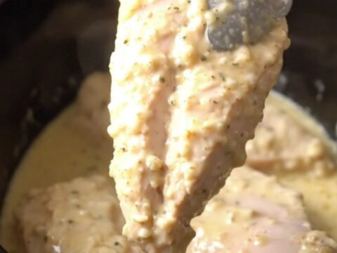 A close-up view of tender cooked parmesan chicken breasts topped with a creamy garlic sauce in a slow cooker.