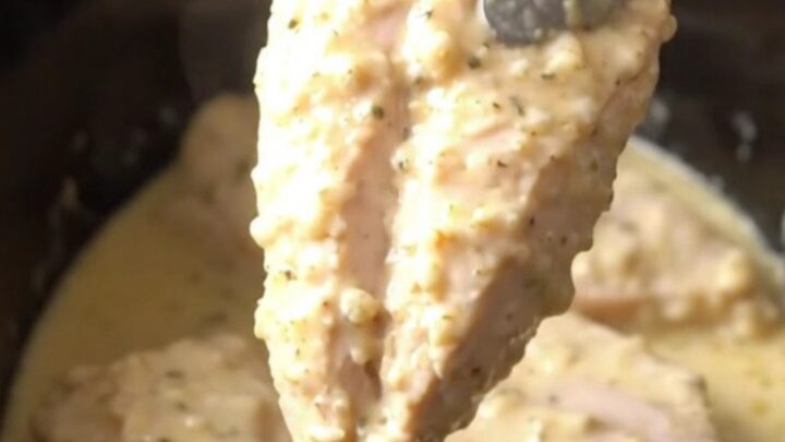 A close-up view of tender cooked parmesan chicken breasts topped with a creamy garlic sauce in a slow cooker.
