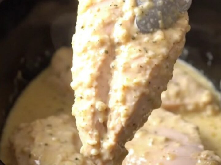 A close-up view of tender cooked parmesan chicken breasts topped with a creamy garlic sauce in a slow cooker.