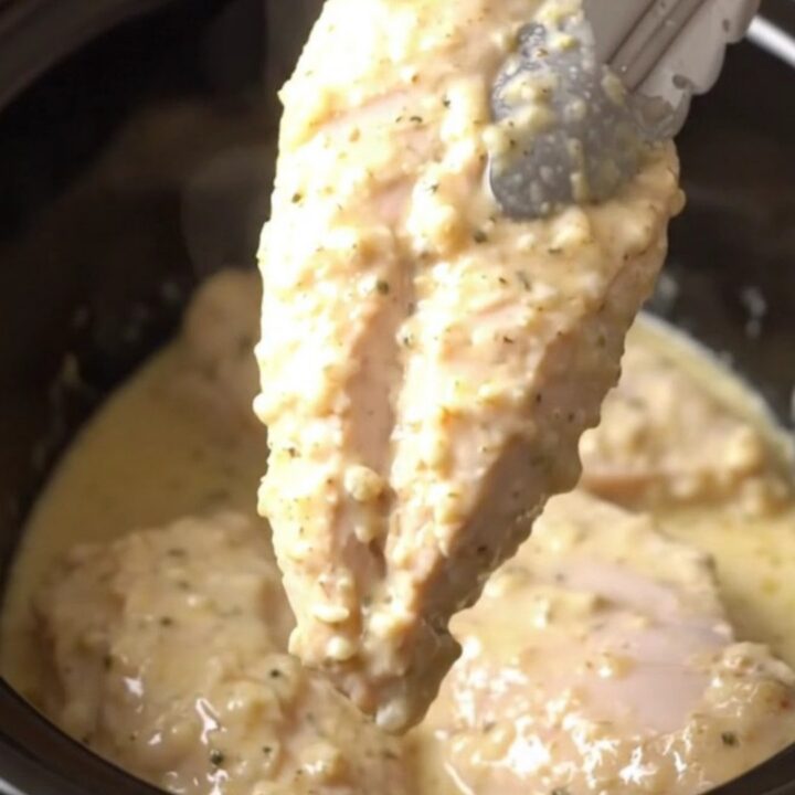 A close-up view of tender cooked parmesan chicken breasts topped with a creamy garlic sauce in a slow cooker.