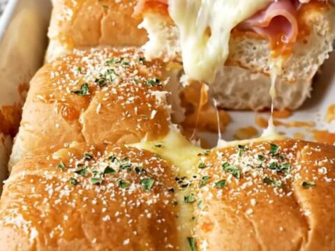A close-up of Hawaiian pizza sliders in a ceramic baking dish with golden brown tops.