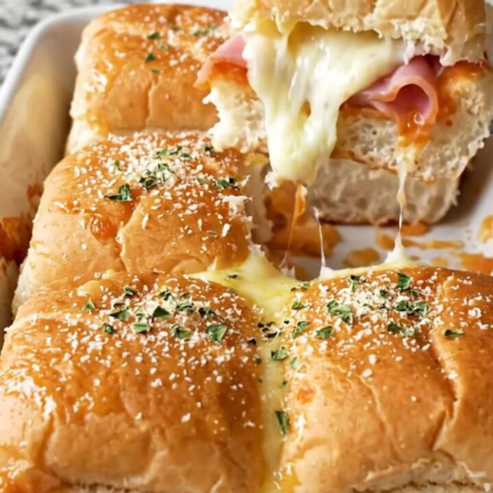 A close-up of Hawaiian pizza sliders in a ceramic baking dish with golden brown tops.