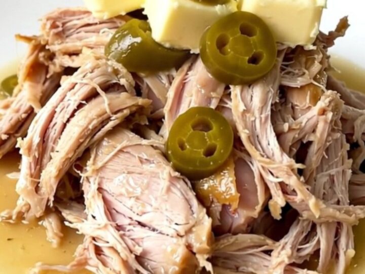 A close-up of a slow cooker filled with a cooked turkey breast, pepperoncini, and rich gravy.