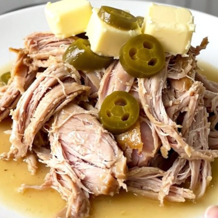 A close-up of a slow cooker filled with a cooked turkey breast, pepperoncini, and rich gravy.