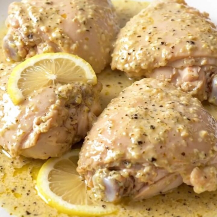 A close-up of tender, creamy lemon pepper chicken thighs served on a white plate.