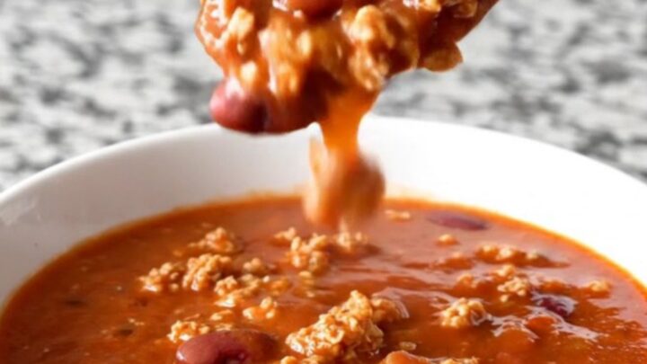 A close-up shot of a white bowl filled with thick, hearty ground turkey and kidney bean chili with light steam rising.