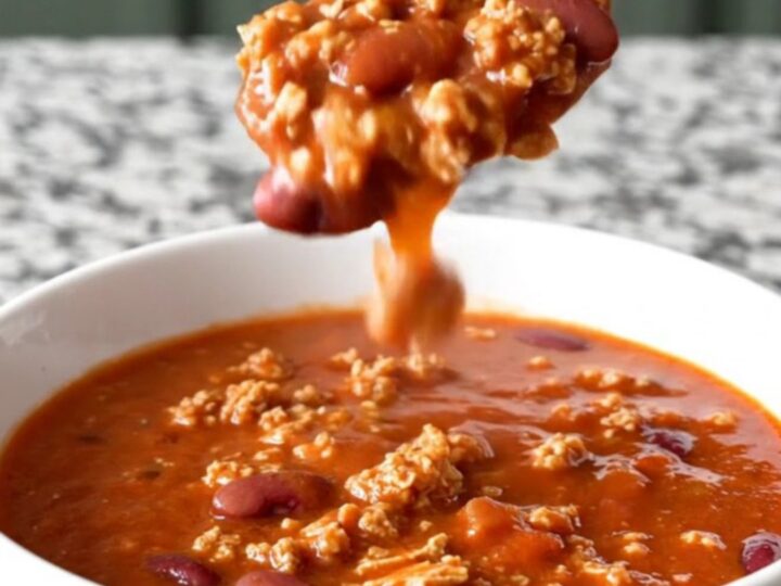 A close-up shot of a white bowl filled with thick, hearty ground turkey and kidney bean chili with light steam rising.