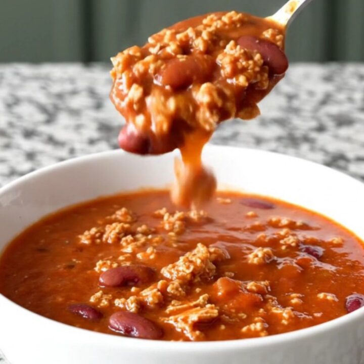 A close-up shot of a white bowl filled with thick, hearty ground turkey and kidney bean chili with light steam rising.