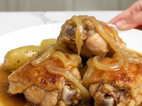 A slow cooker filled with tender chicken thighs, halved baby gold potatoes, and a rich onion-based gravy.