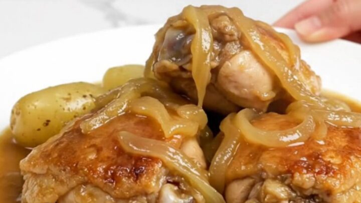 A slow cooker filled with tender chicken thighs, halved baby gold potatoes, and a rich onion-based gravy.
