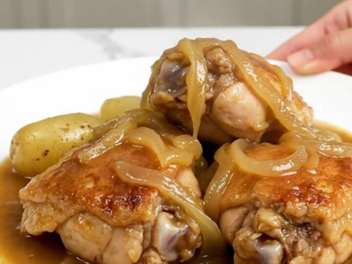 A slow cooker filled with tender chicken thighs, halved baby gold potatoes, and a rich onion-based gravy.