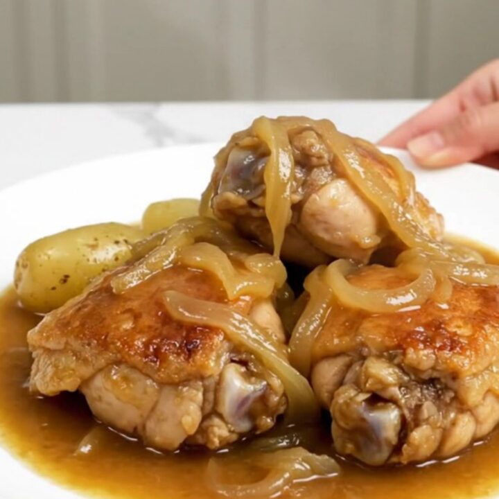 A slow cooker filled with tender chicken thighs, halved baby gold potatoes, and a rich onion-based gravy.