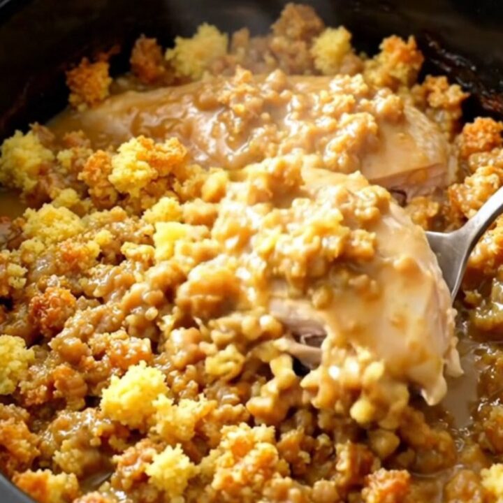A close-up of slow cooker chicken breasts topped with savory stuffing and gravy in a black ceramic bowl.