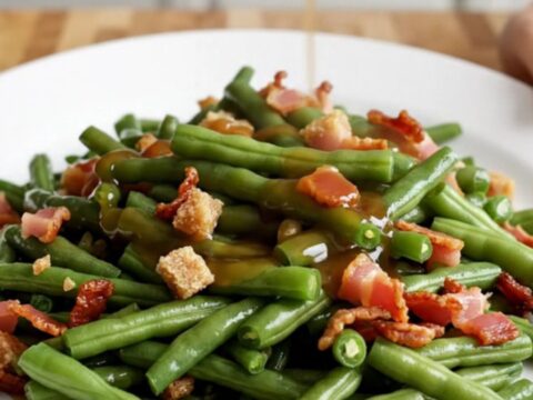 A close-up of tender green beans in a slow cooker, glazed in a brown sugar and soy butter sauce with crispy bacon bits.