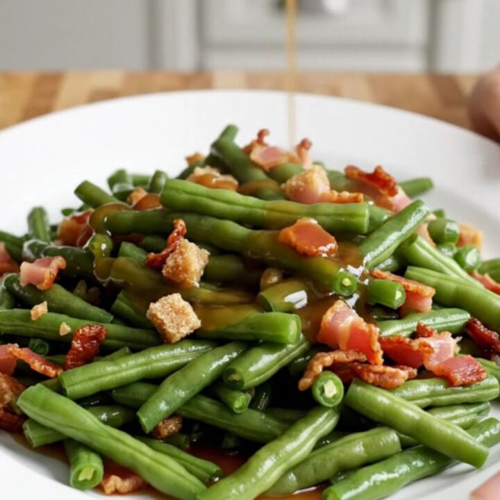 A close-up of tender green beans in a slow cooker, glazed in a brown sugar and soy butter sauce with crispy bacon bits.