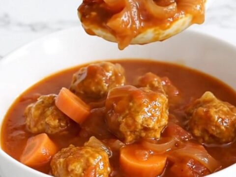 A white bowl filled with turkey meatballs, halved baby potatoes, and carrot coins in a thick, savory tomato-onion gravy.