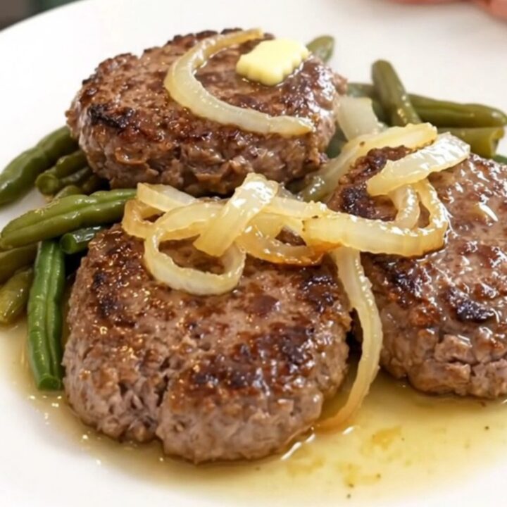 Four slow-cooked beef patties with green beans and halved baby potatoes in a slow cooker.