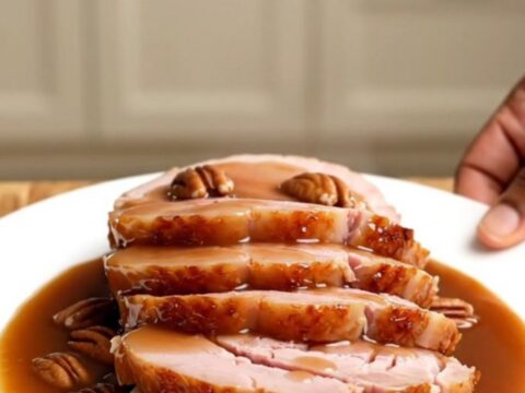 A beautifully glazed spiral-sliced ham in a white slow cooker, topped with pecans and a rich praline sauce.