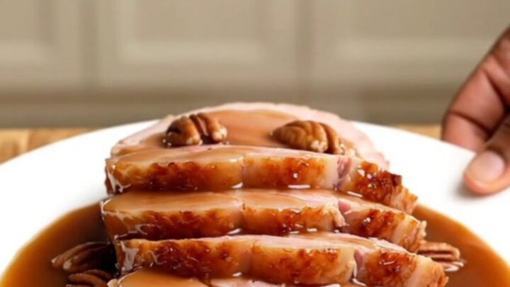 A beautifully glazed spiral-sliced ham in a white slow cooker, topped with pecans and a rich praline sauce.