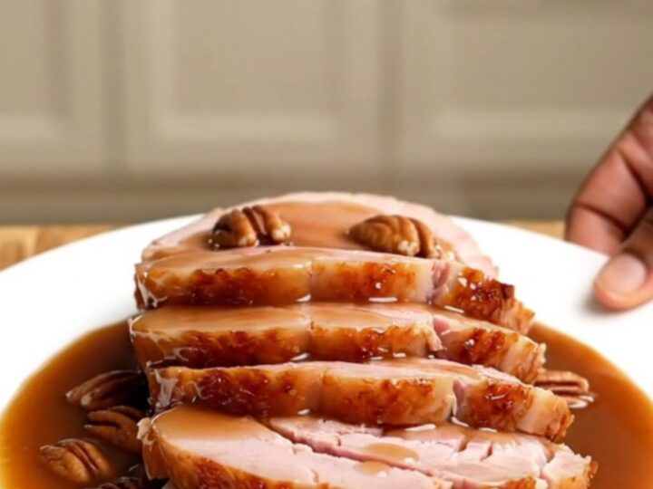 A beautifully glazed spiral-sliced ham in a white slow cooker, topped with pecans and a rich praline sauce.