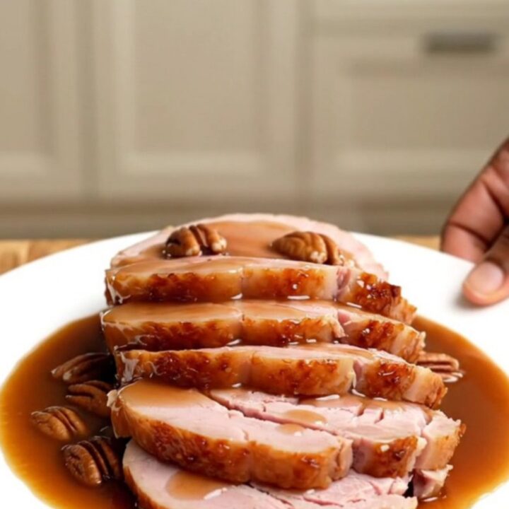 A beautifully glazed spiral-sliced ham in a white slow cooker, topped with pecans and a rich praline sauce.