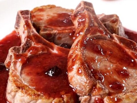A top-down view of thick-cut pork chops arranged in a slow cooker, topped with grape jelly and chili sauce.