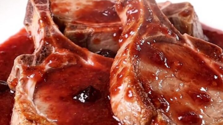 A top-down view of thick-cut pork chops arranged in a slow cooker, topped with grape jelly and chili sauce.