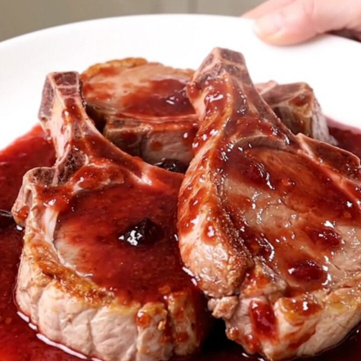 A top-down view of thick-cut pork chops arranged in a slow cooker, topped with grape jelly and chili sauce.