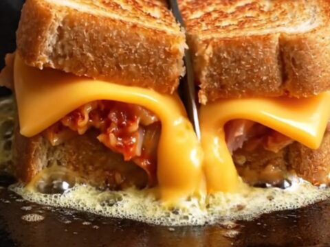 A close-up of a golden-brown tuna melt with a visible sesame seed crust, oozing with melted sharp cheddar cheese.