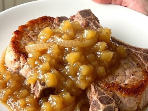 A close-up of tender bone-in pork chops topped with chunky applesauce and caramelized onions in a slow cooker.