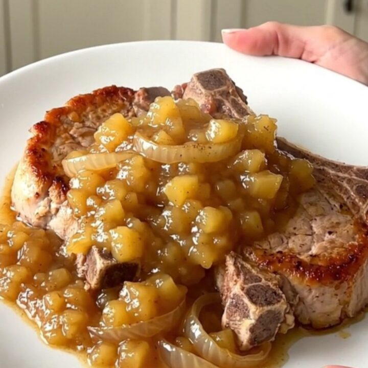A close-up of tender bone-in pork chops topped with chunky applesauce and caramelized onions in a slow cooker.